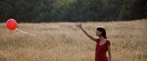 A young woman standing in a field letting go of a red balloon